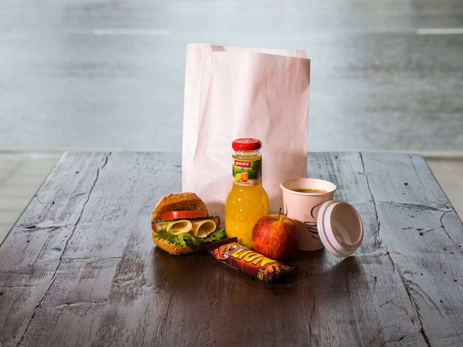 Un repas composé d’un hamburger, d’une pomme, d’un jus de fruits et d’une collation, le tout servi sur une table en bois.