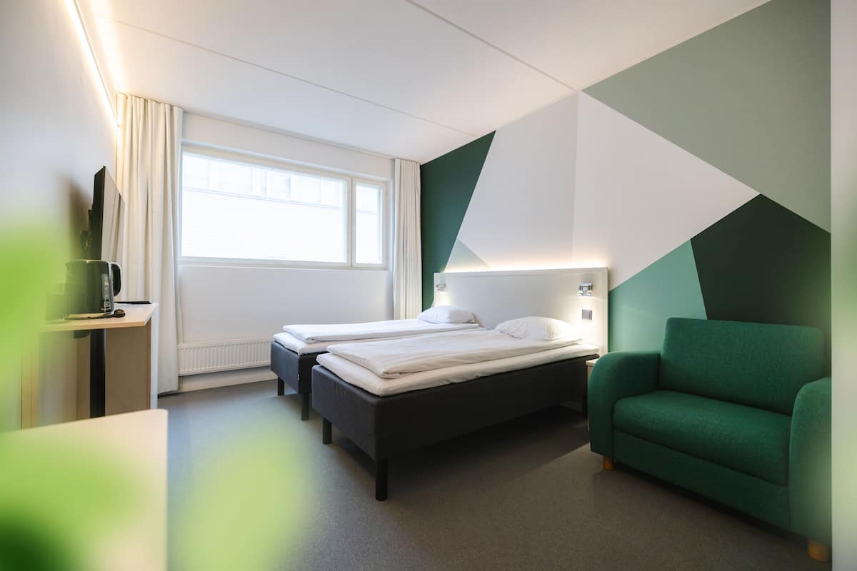 A hotel room with two beds, a green sofa, a desk with a computer, and a window with curtains.
