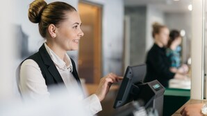 Een hotel receptie met een baliemedewerker achter een computer, een balie en een glazen scheidingswand.