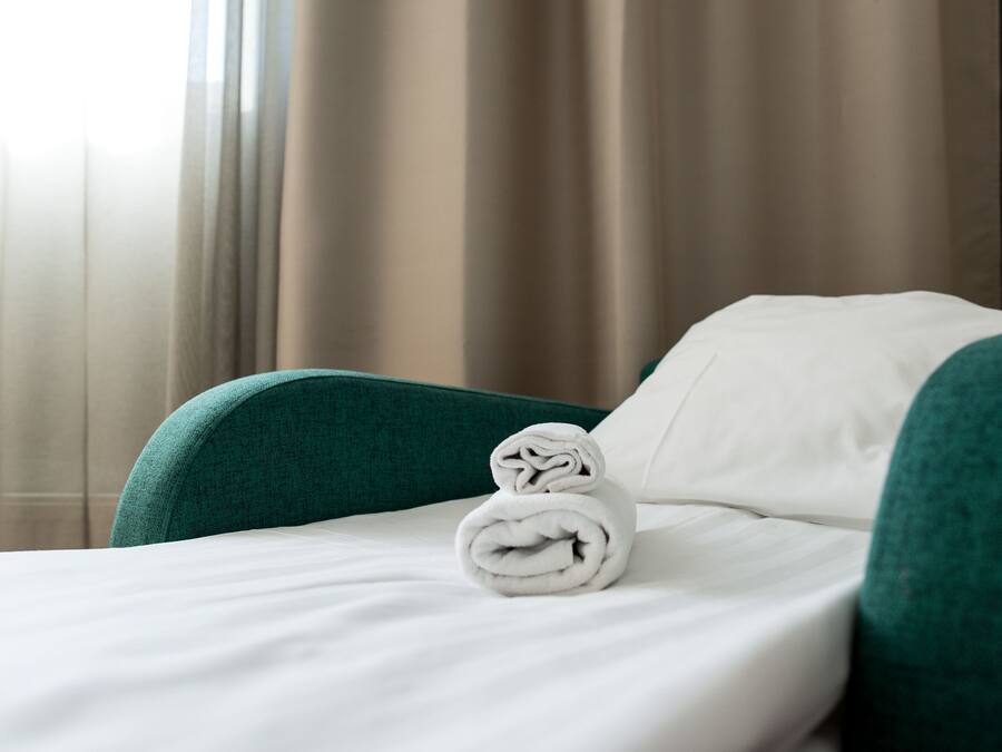 A neatly made bed with a rolled towel, green upholstered headboard, and white bedding.