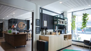 Een moderne hotelentree met een receptiebalie, een groene mat met de tekst 'GreenStar Hotel', een zithoek en uitzicht op de straat door grote ramen.