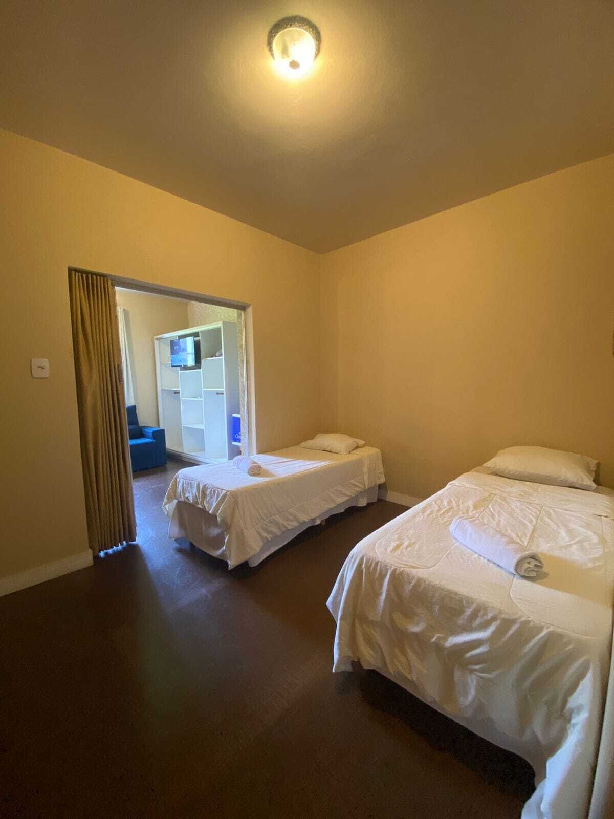Une chambre d’hôtel avec deux lits simples, une armoire et une salle de bain visible à travers une porte ouverte.