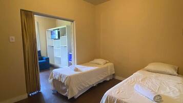 A hotel room with two single beds, a wardrobe, and a bathroom visible through an open door.