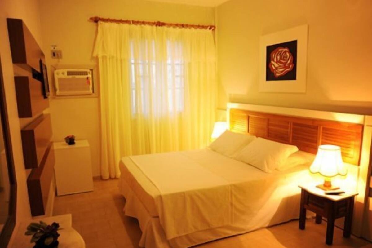 A hotel room with a bed, bedside table, lamp, and a wall-mounted air conditioner.