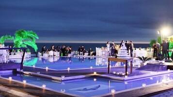 Un área junto a la piscina con varias piscinas, un escenario para eventos y vistas al mar.