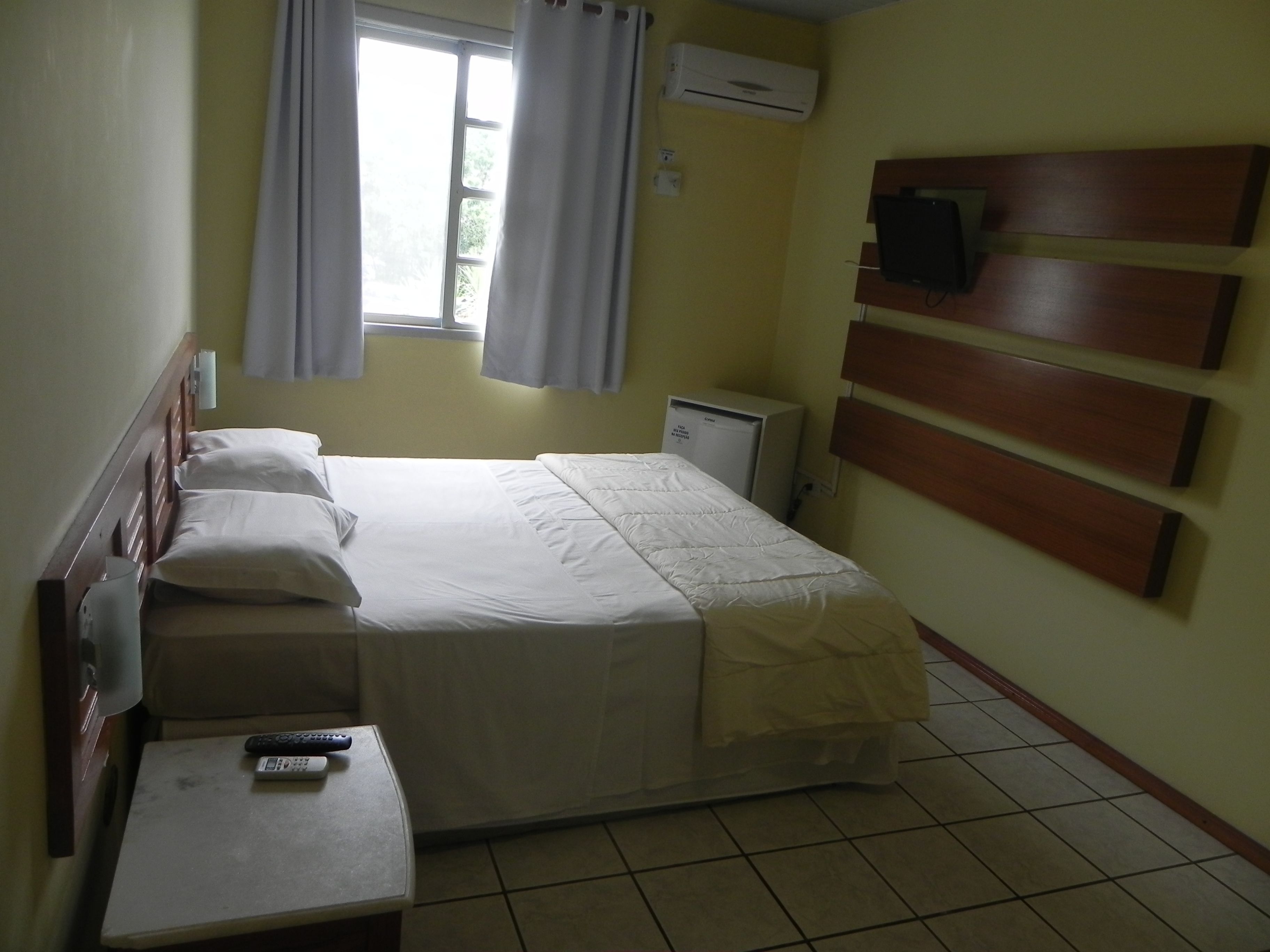 Una habitación de hotel con cama, escritorio, televisión y aire acondicionado.