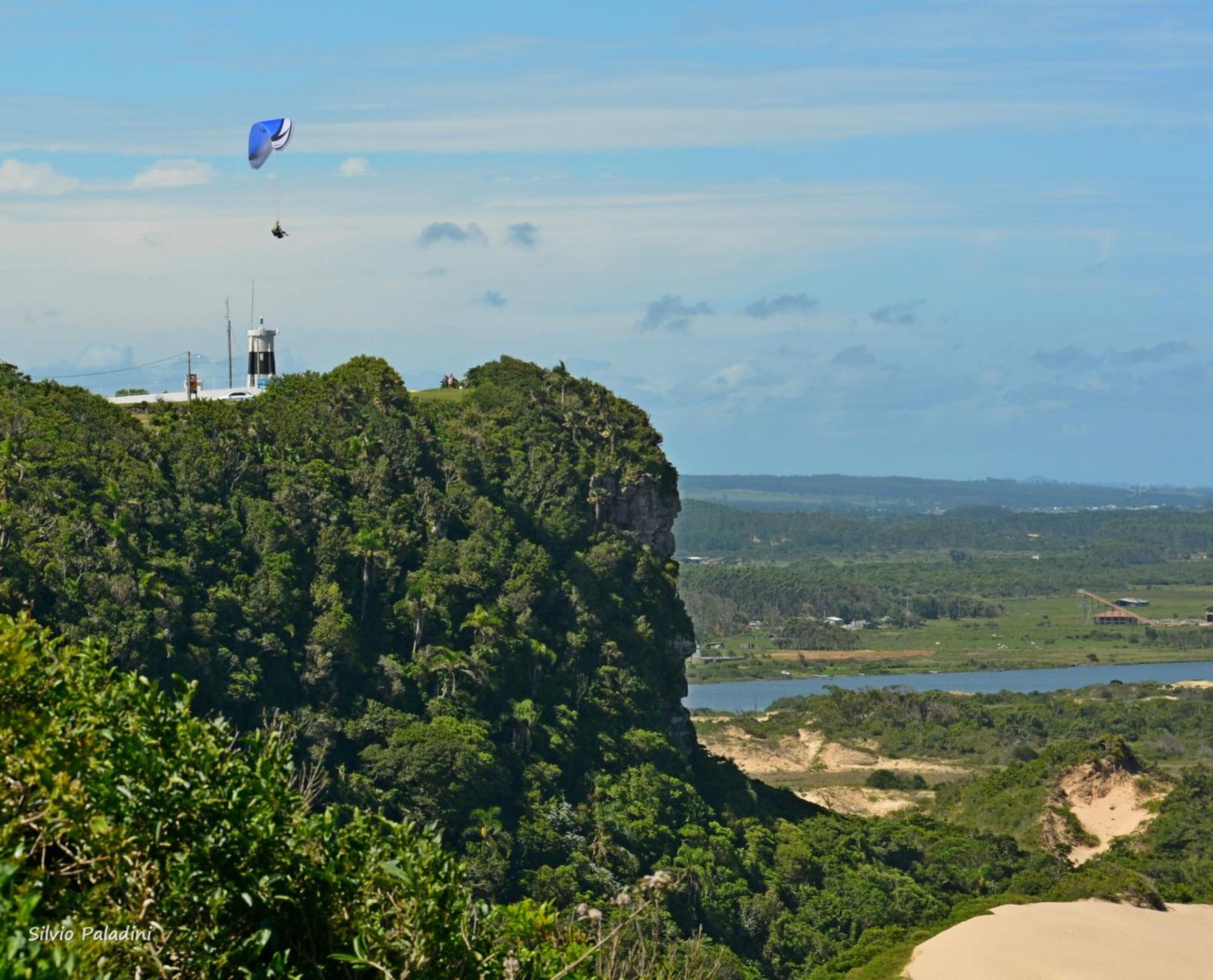 Paisagem costeira com penhasco, vegetação e um corpo de água.