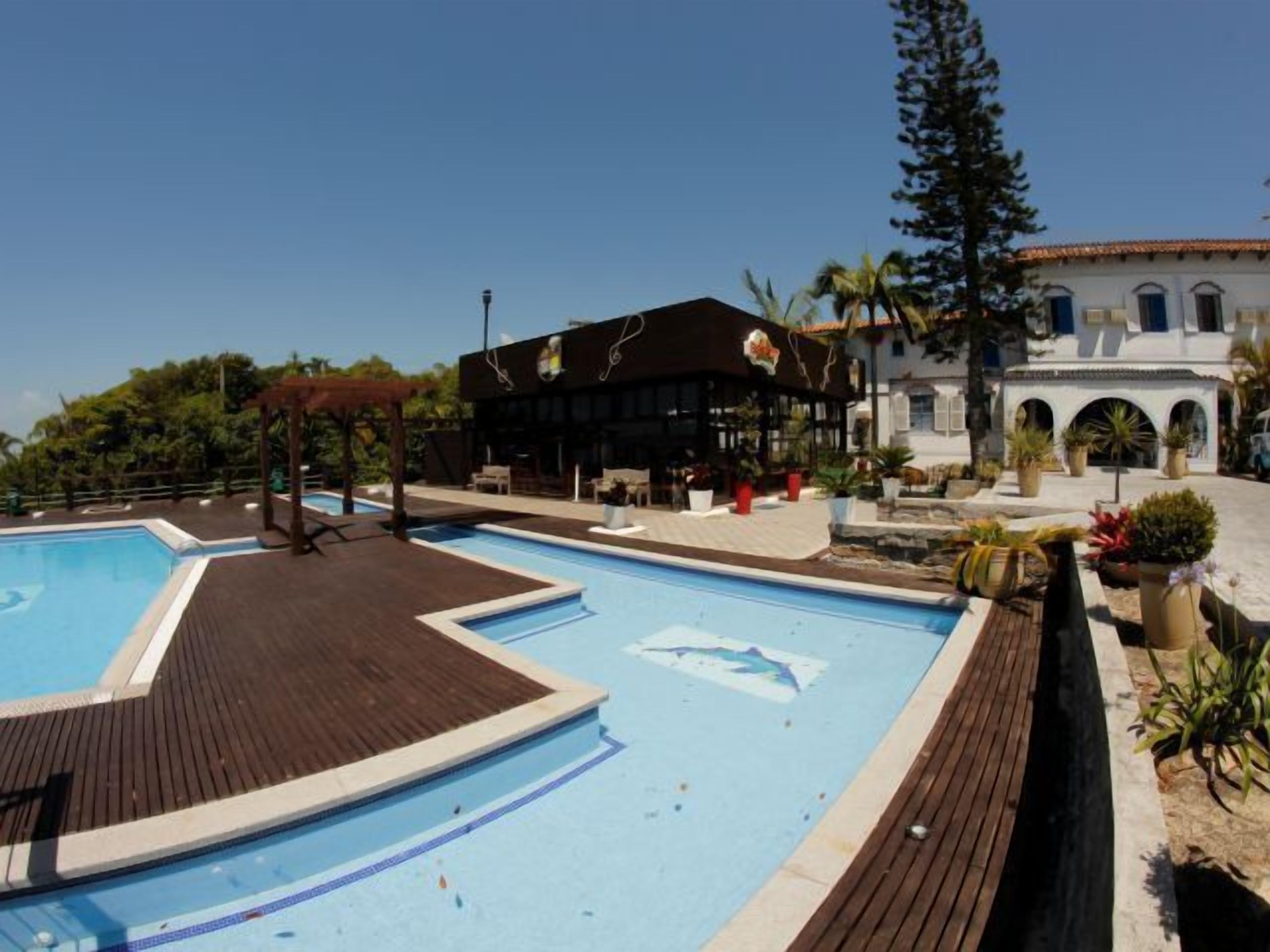 A swimming pool with wooden deck, a covered seating area, and a building with outdoor seating.
