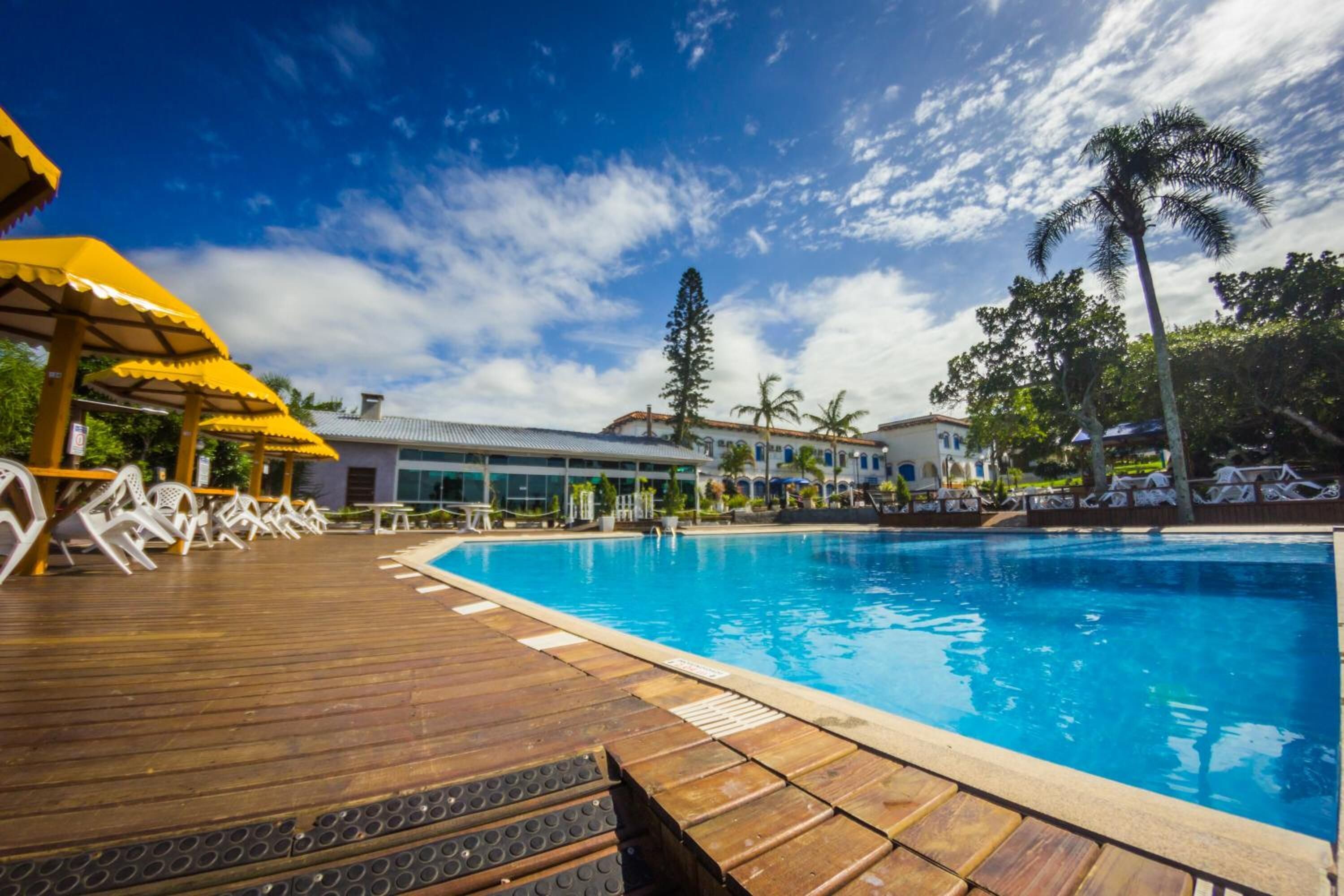 Un área de piscina con cubierta de madera, sillas de descanso y sombrillas.