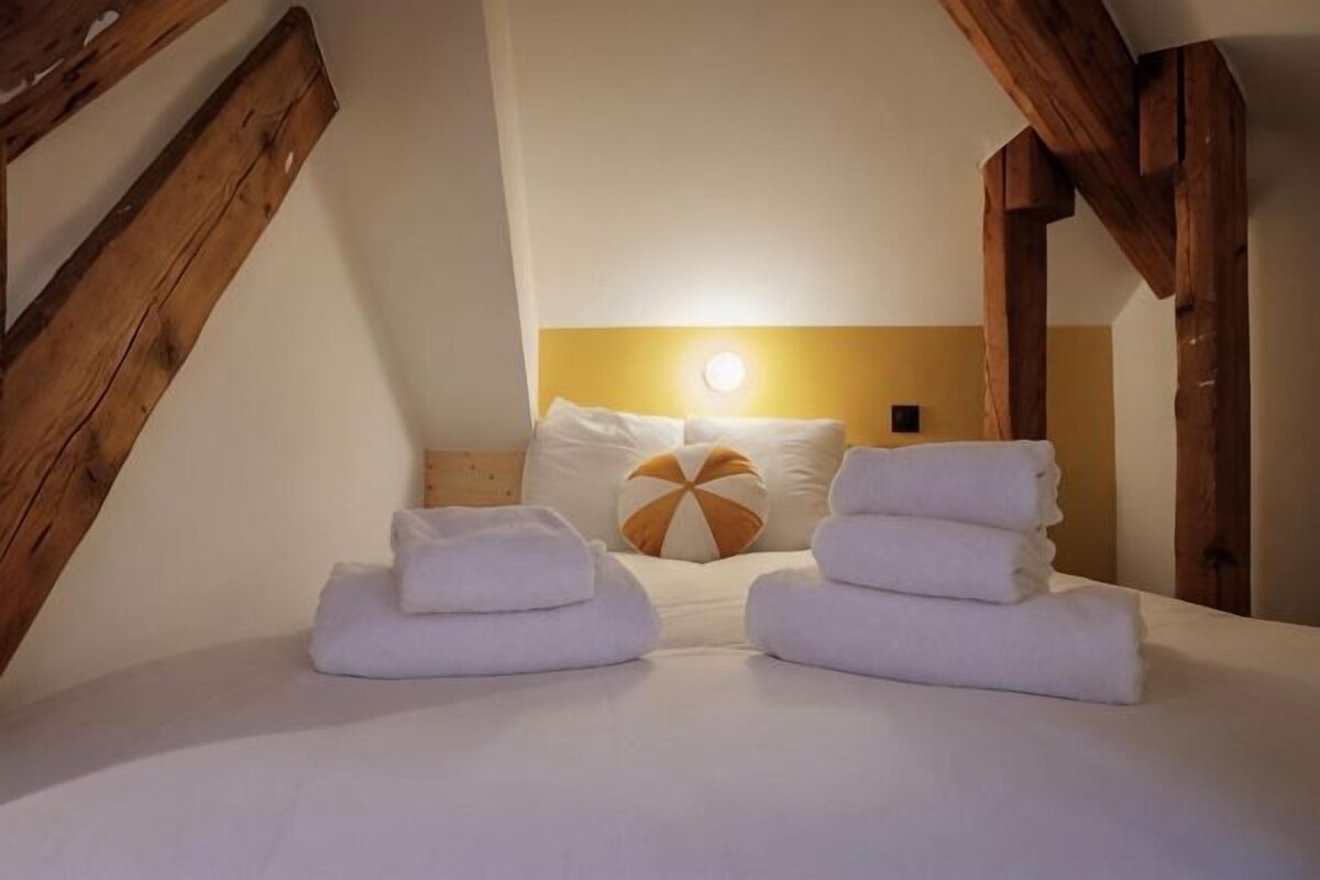 Un dormitorio con techo inclinado, cama con ropa blanca y cabecera de madera.