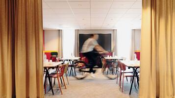 A room with tables and chairs arranged for dining, a large window, and curtains.