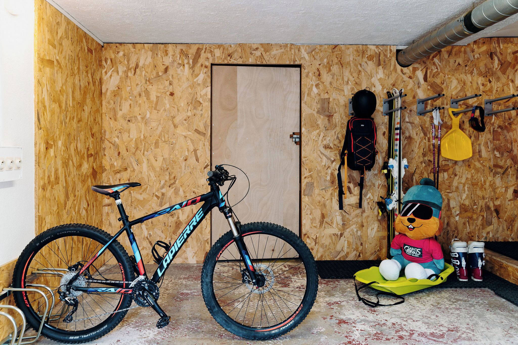 Une pièce avec un mur en bois, une porte, un vélo et un jouet en peluche.