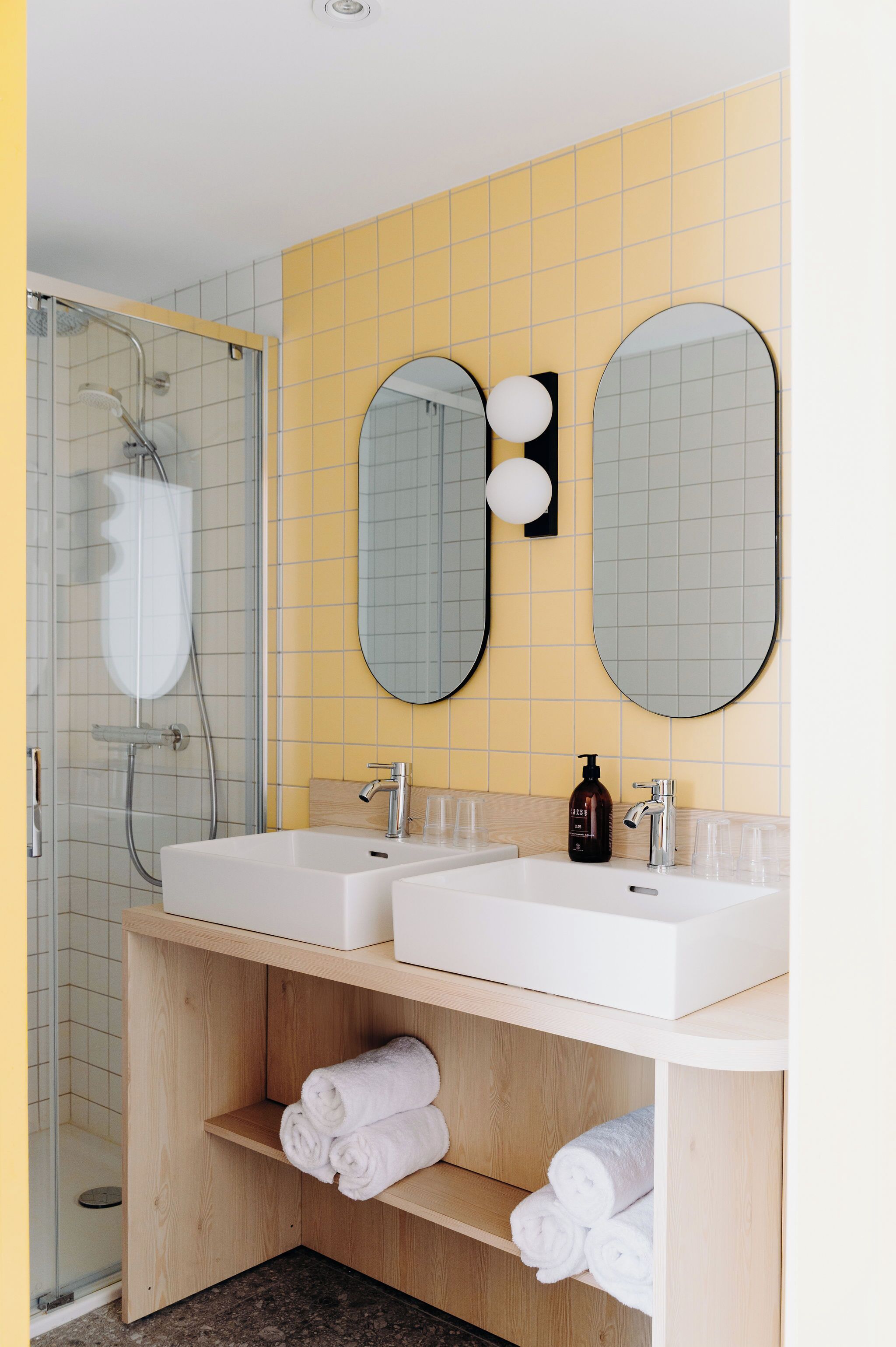 Un bagno moderno con due lavandini, una doccia e un mobile vanitario in legno con asciugamani.