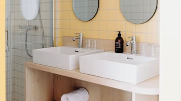 Un bagno moderno con due lavandini, una doccia e un mobile vanitario in legno con asciugamani.