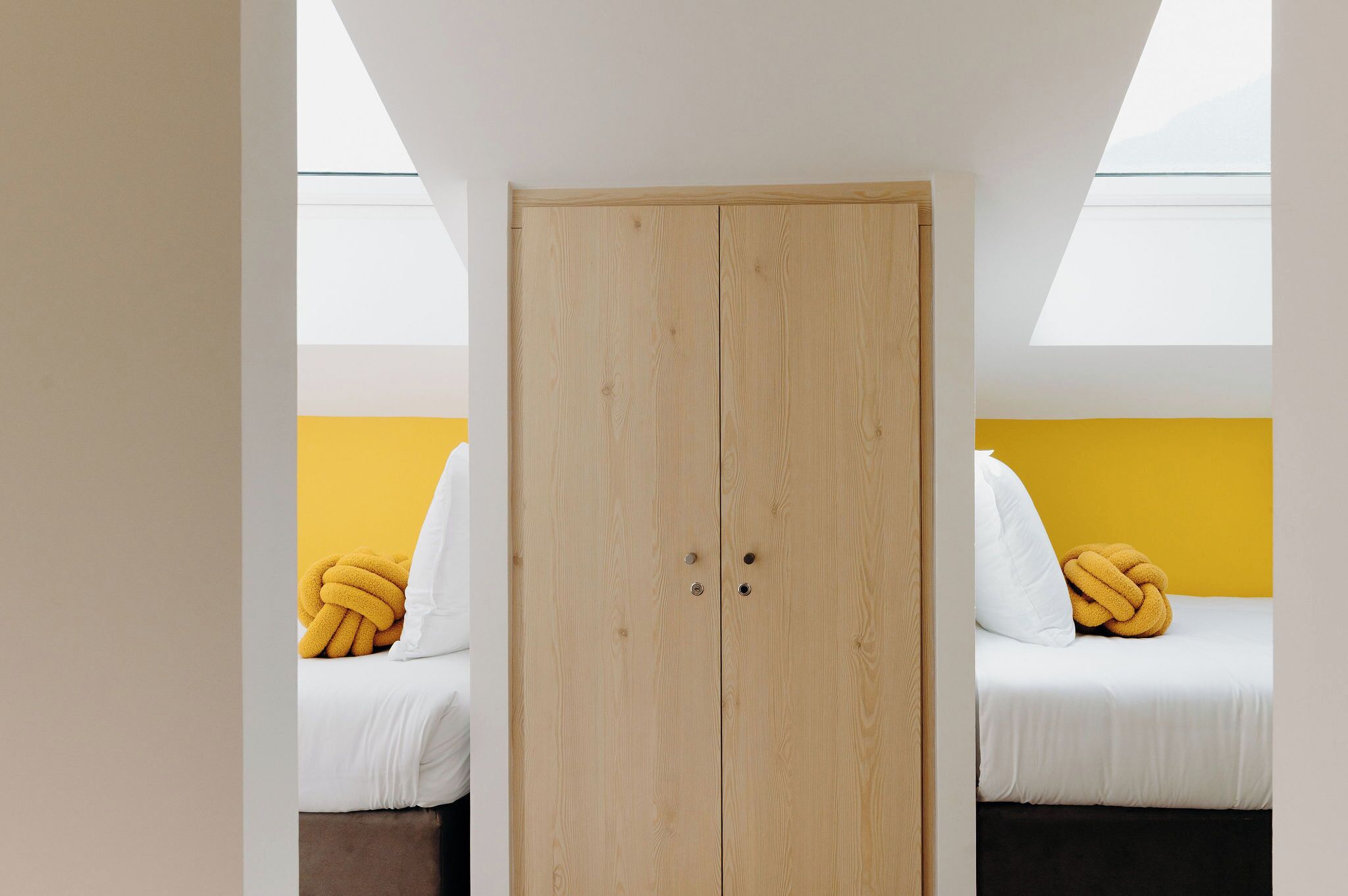 Una habitación con un armario de madera, dos camas con ropa de cama amarilla y blanca, y un tragaluz.