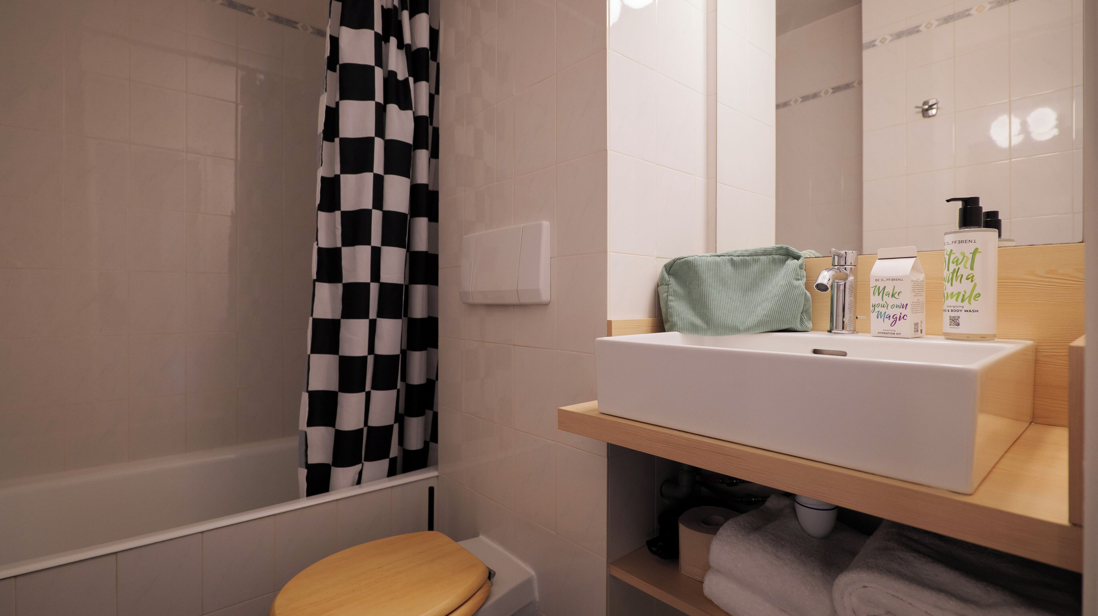 Une salle de bain moderne avec un rideau de douche à carreaux, un lavabo blanc et un miroir au-dessus.