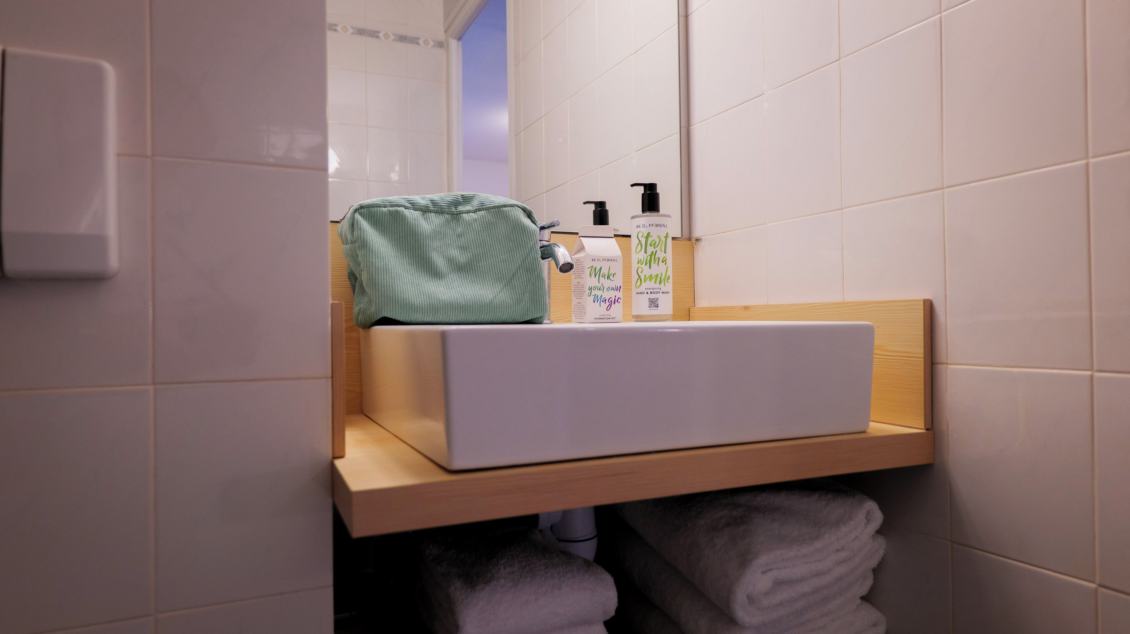 A bathroom with a white sink, a green towel, and two bottles of hand soap on a wooden shelf.