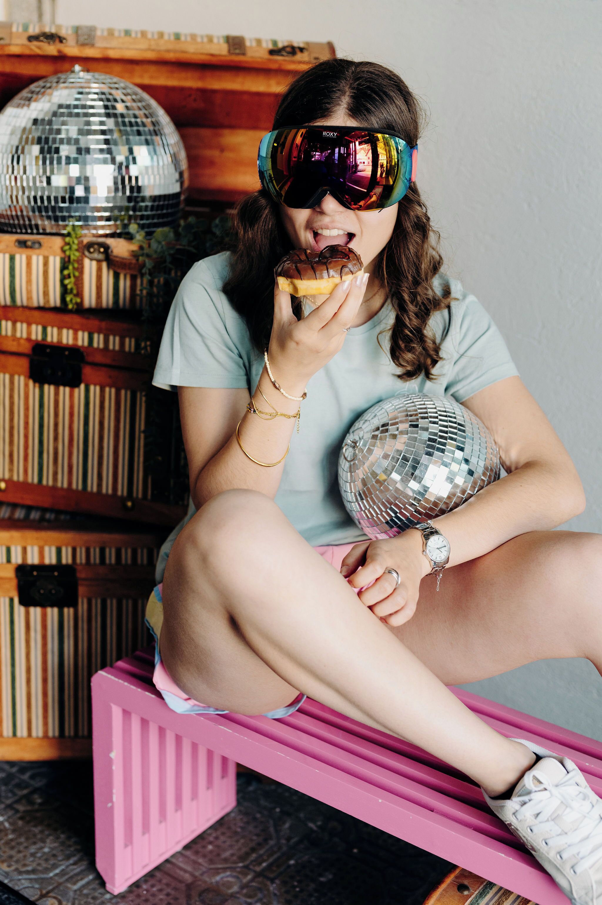 Une personne assise sur un banc rose, avec une boule à facettes et des étagères à livres en arrière-plan.