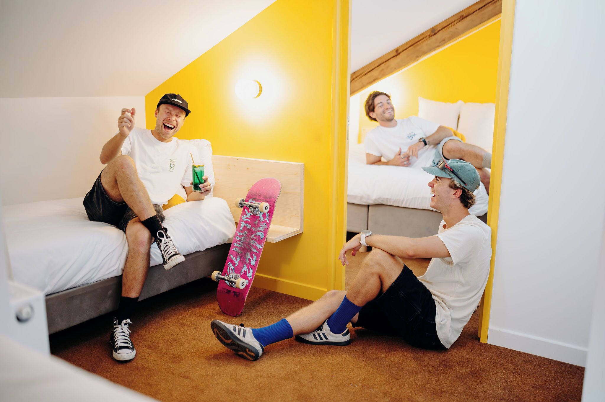 A room with a bed, a skateboard, and a person sitting on the floor.