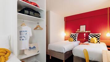 Quarto de hotel com duas camas, um guarda-roupa e uma parede de destaque vermelha.