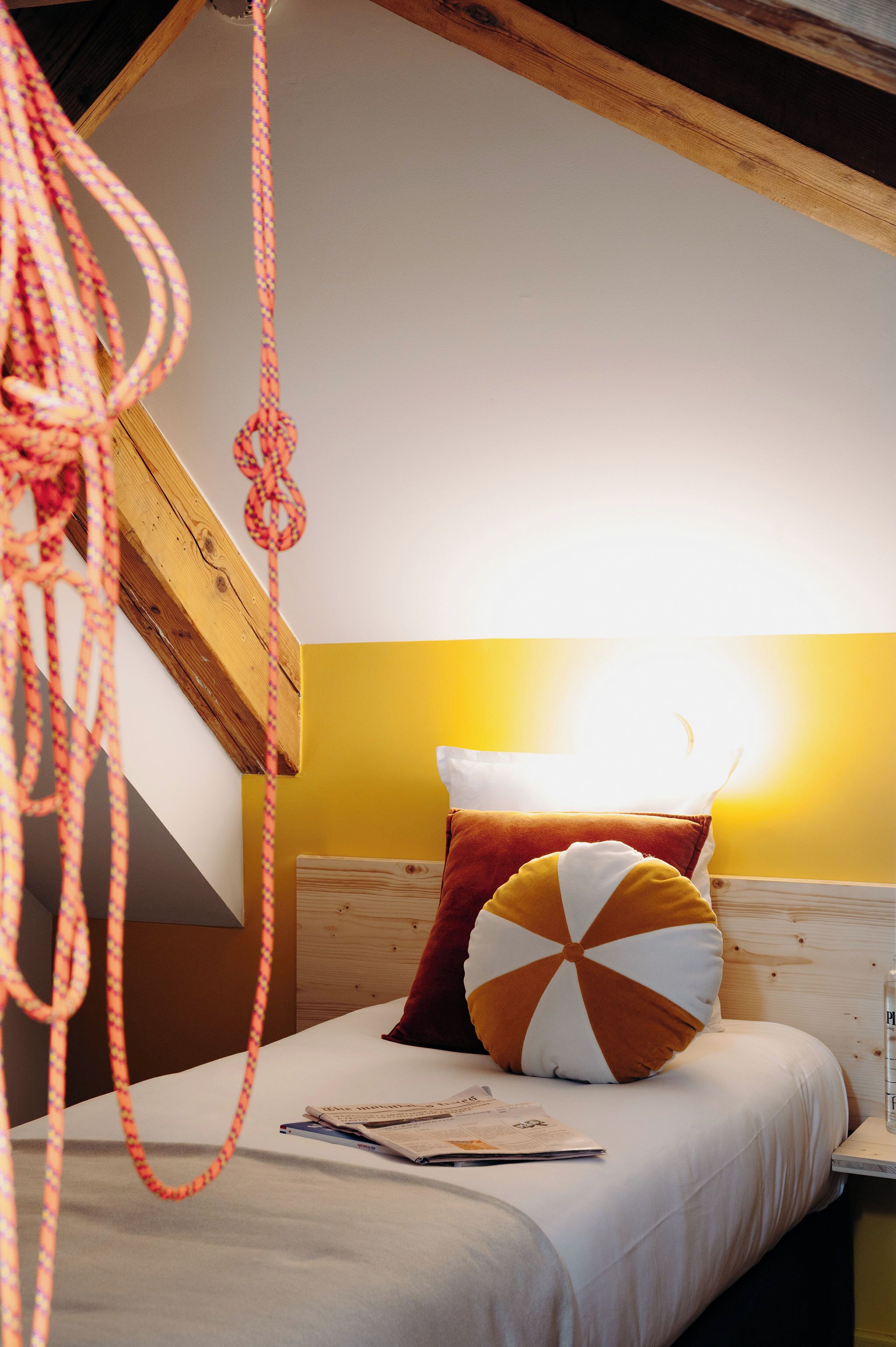 Un dormitorio con techo de madera, una cama con almohada blanca y naranja, y una cuerda colgante.