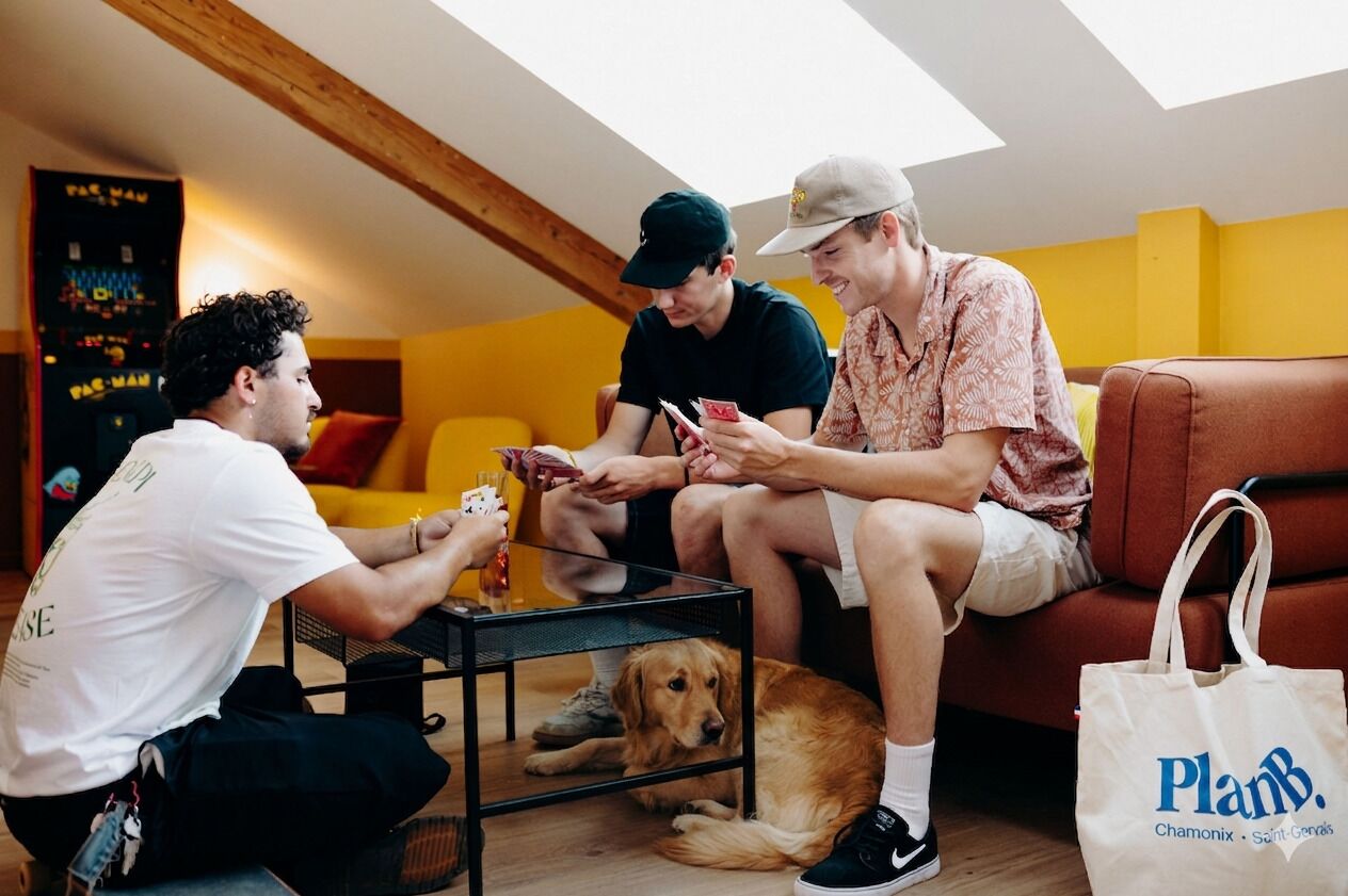 Three people seated on a couch with a dog, a table with cards, and a Planb bag.