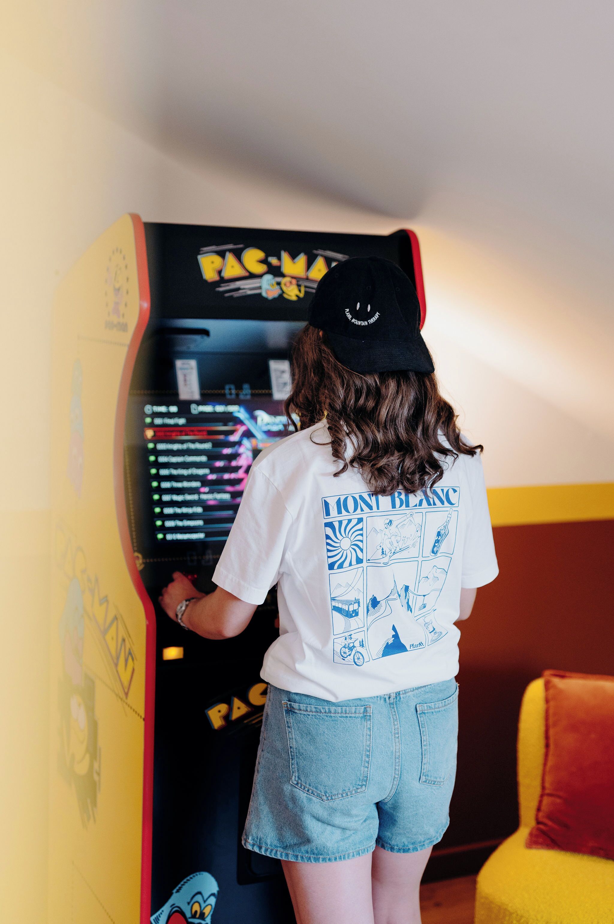 A person playing a Pac-Man game in a room with yellow walls and a red and yellow chair.