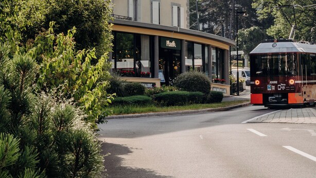 A building with a curved facade, a sign that reads "Hotel", and a tram in the foreground. - PlanB Hotel - Living Saint Gervais (Saint-Gervais-les-Bains)