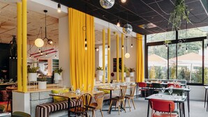 A restaurant with high ceilings, yellow curtains, and hanging disco balls. Tables are set with glasses and cutlery. - PlanB Hotel - Living Saint Gervais (Saint-Gervais-les-Bains)