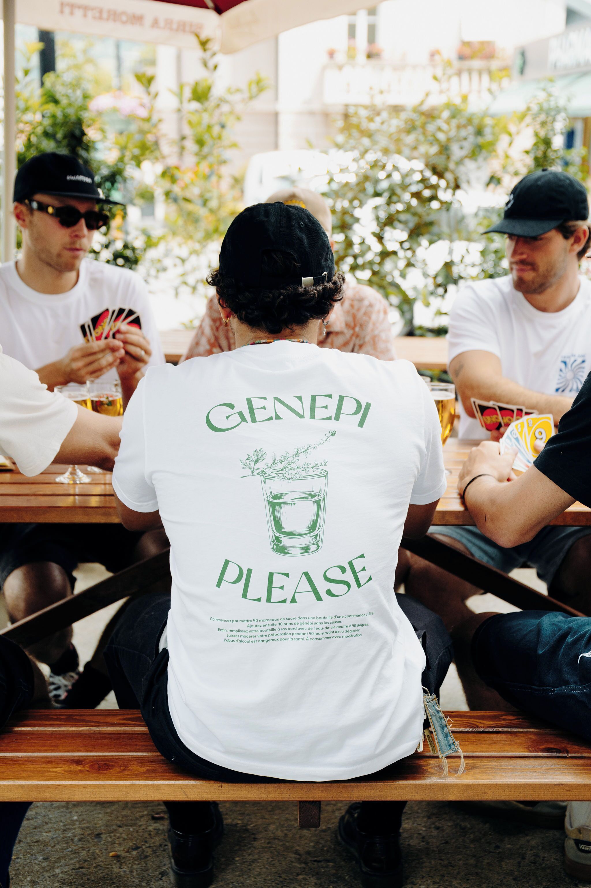 A group of people sitting at an outdoor table, engaged in a card game.