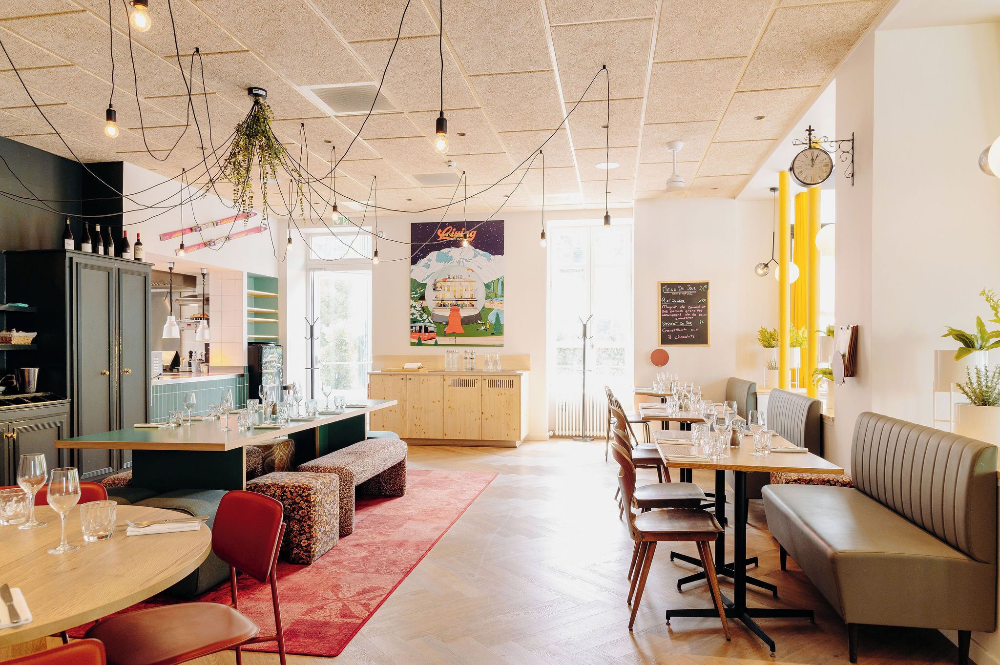 A modern restaurant with a central island, wooden tables, and a seating area with benches.