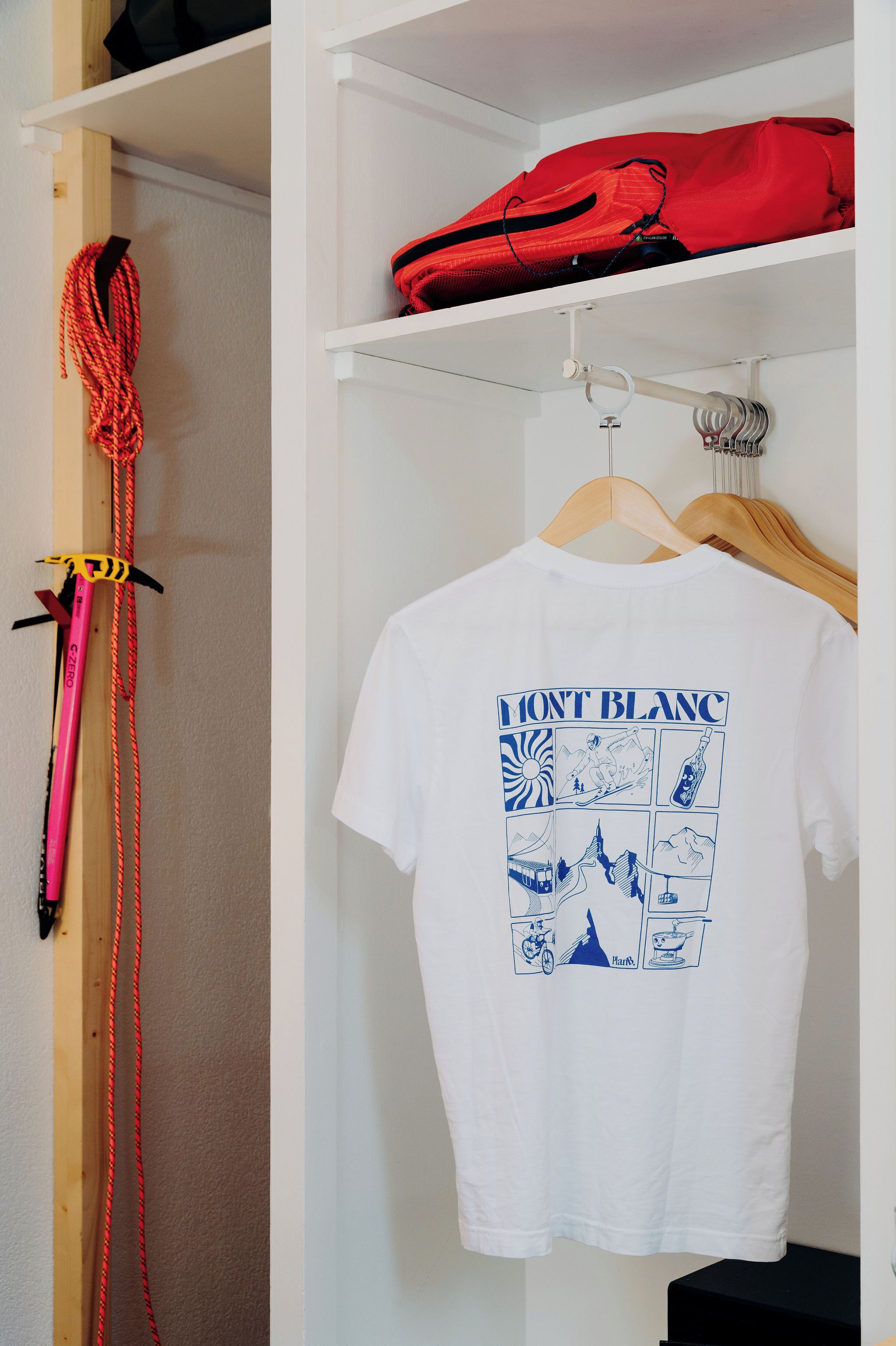 A white T-shirt with a blue graphic design hanging on a wooden hanger in a closet.