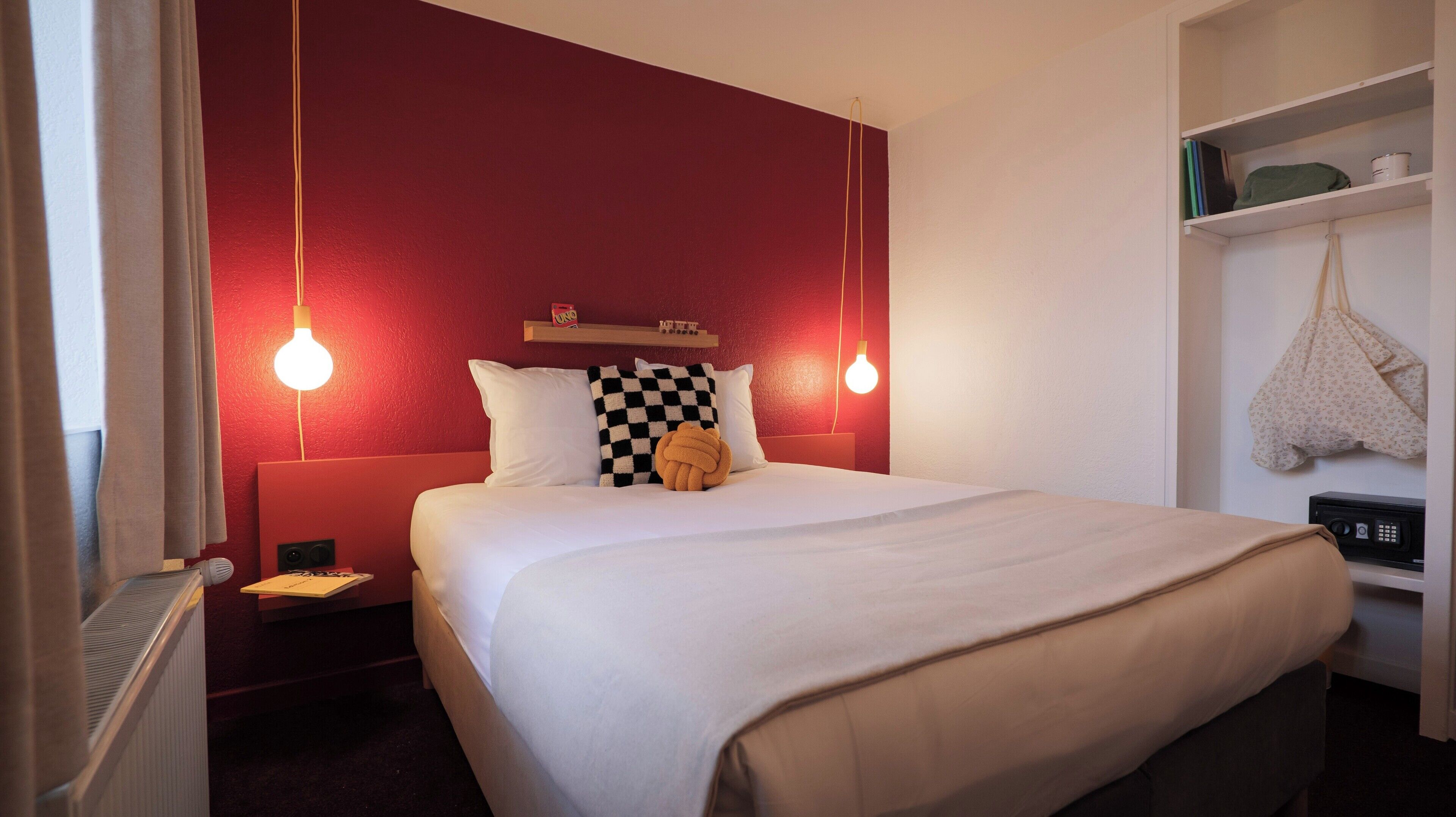 Camera d'albergo con un letto grande, due abat-jour, un piccolo ripiano con una bottiglia e un comodino con una lampada.