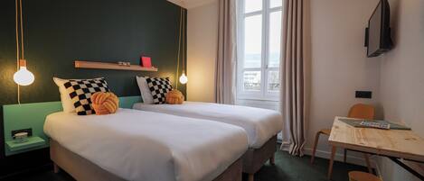 Quarto de hotel com duas camas, uma escrivaninha, uma cadeira, uma televisão e uma janela com cortinas.