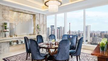 Un área de comedor con vista a la ciudad, que incluye un candelabro, paredes de mármol y un gran ventanal.