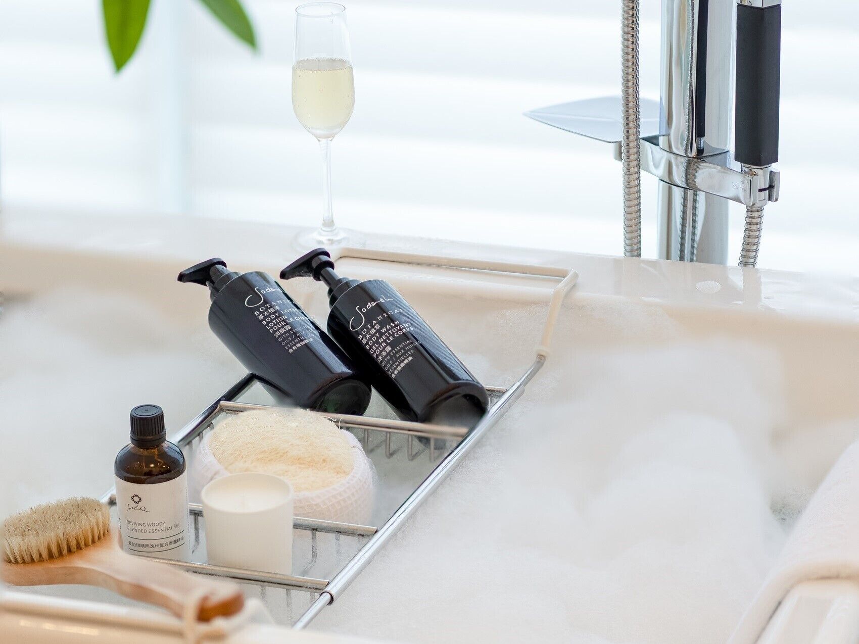 A bathroom with a bathtub, a glass of white wine, and toiletries including body wash and lotion.