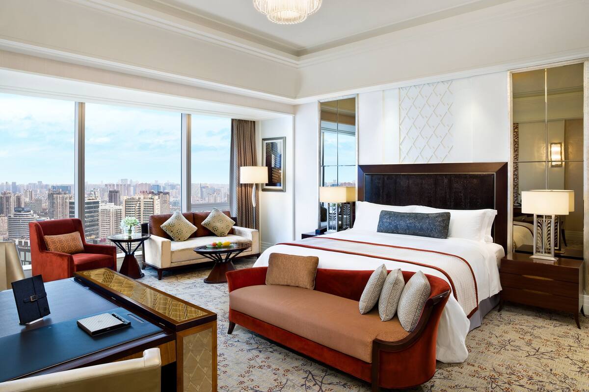 A hotel room with a large bed, a sofa, a desk, and a view of the city.