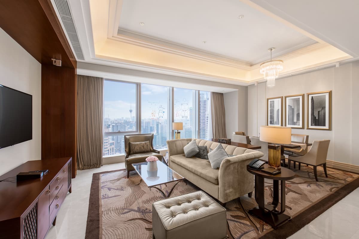 A modern hotel room with a large window offering a city view, a comfortable sofa, a coffee table, and a television.