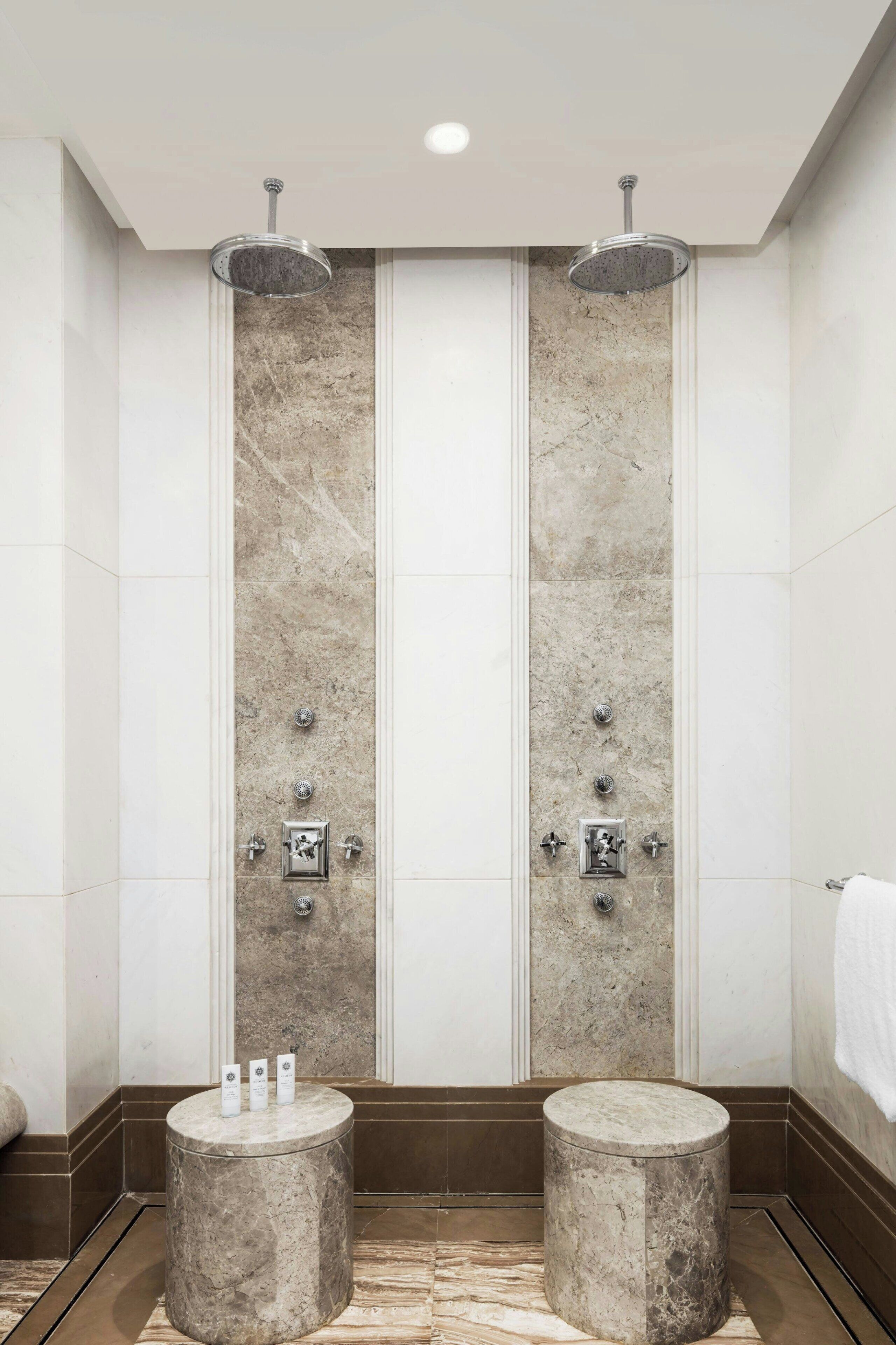 Een moderne badkamer met twee marmeren wastafels, een douche met regendouche en een marmeren vloer.