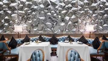 A restaurant with a geometric marble wall, blue upholstered booths, and white tablecloths.
