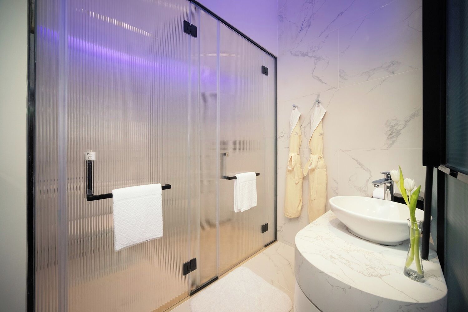 A modern bathroom with a glass shower enclosure, a marble sink, and a mirror.