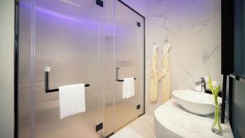 A modern bathroom with a glass shower enclosure, a marble sink, and a mirror.