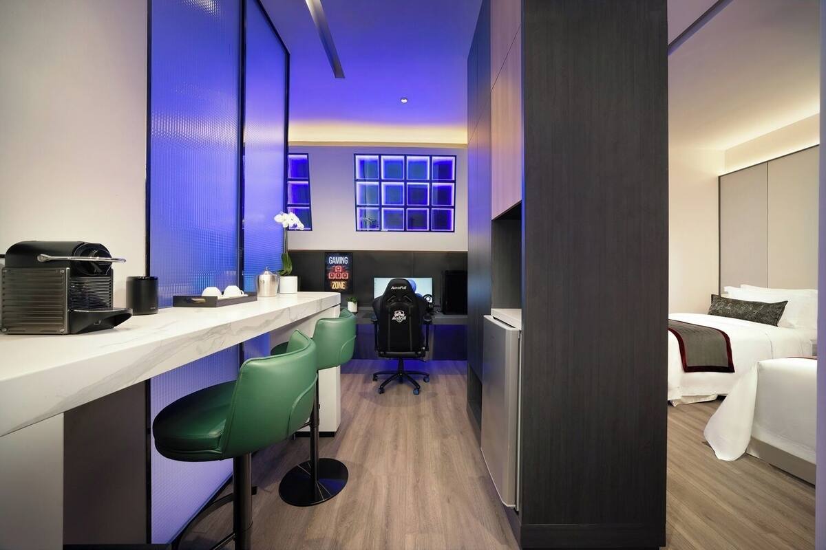 A modern hotel room with a desk, gaming zone, and a bed.