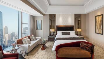 Une chambre d’hôtel avec un grand lit, un canapé, un fauteuil rouge, une table basse en verre et une vue sur le panorama de la ville.
