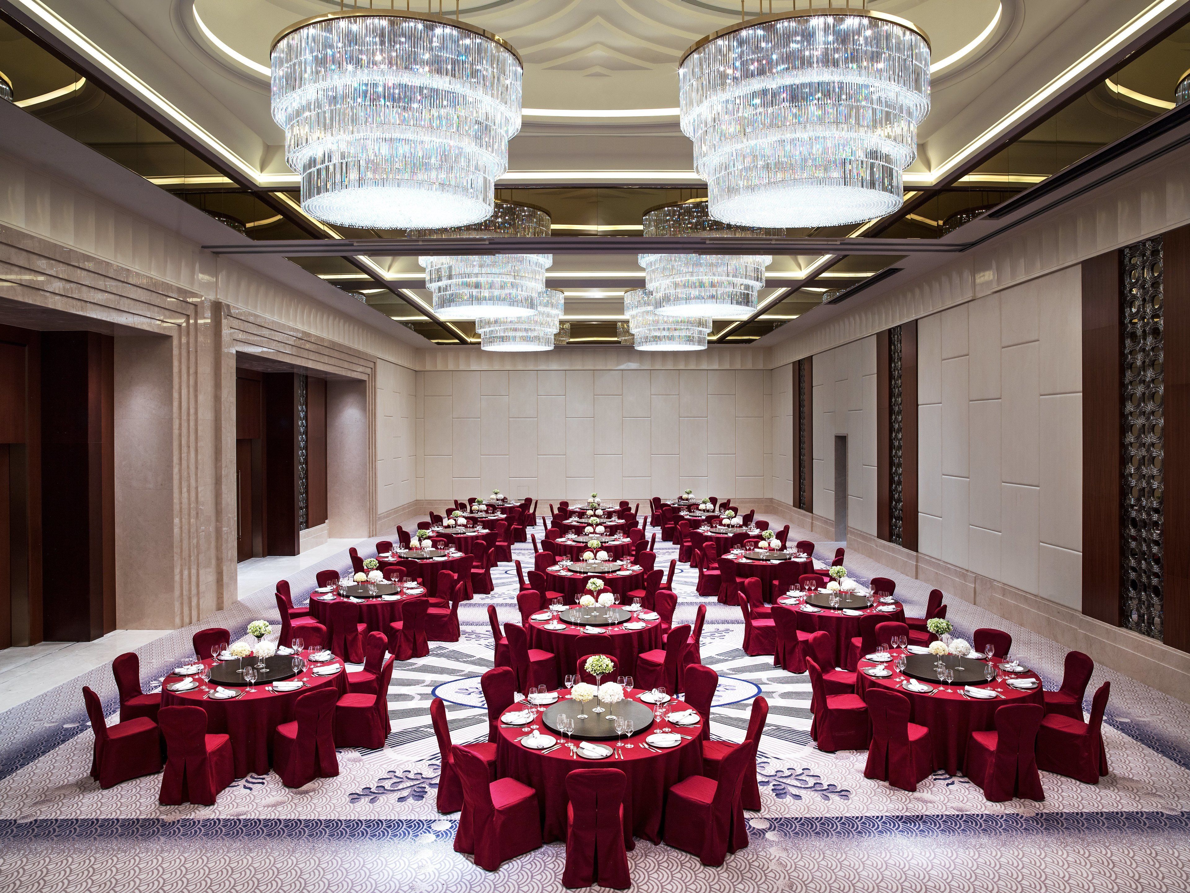 A large conference room with multiple round tables, each set with red chairs and white tablecloths.
