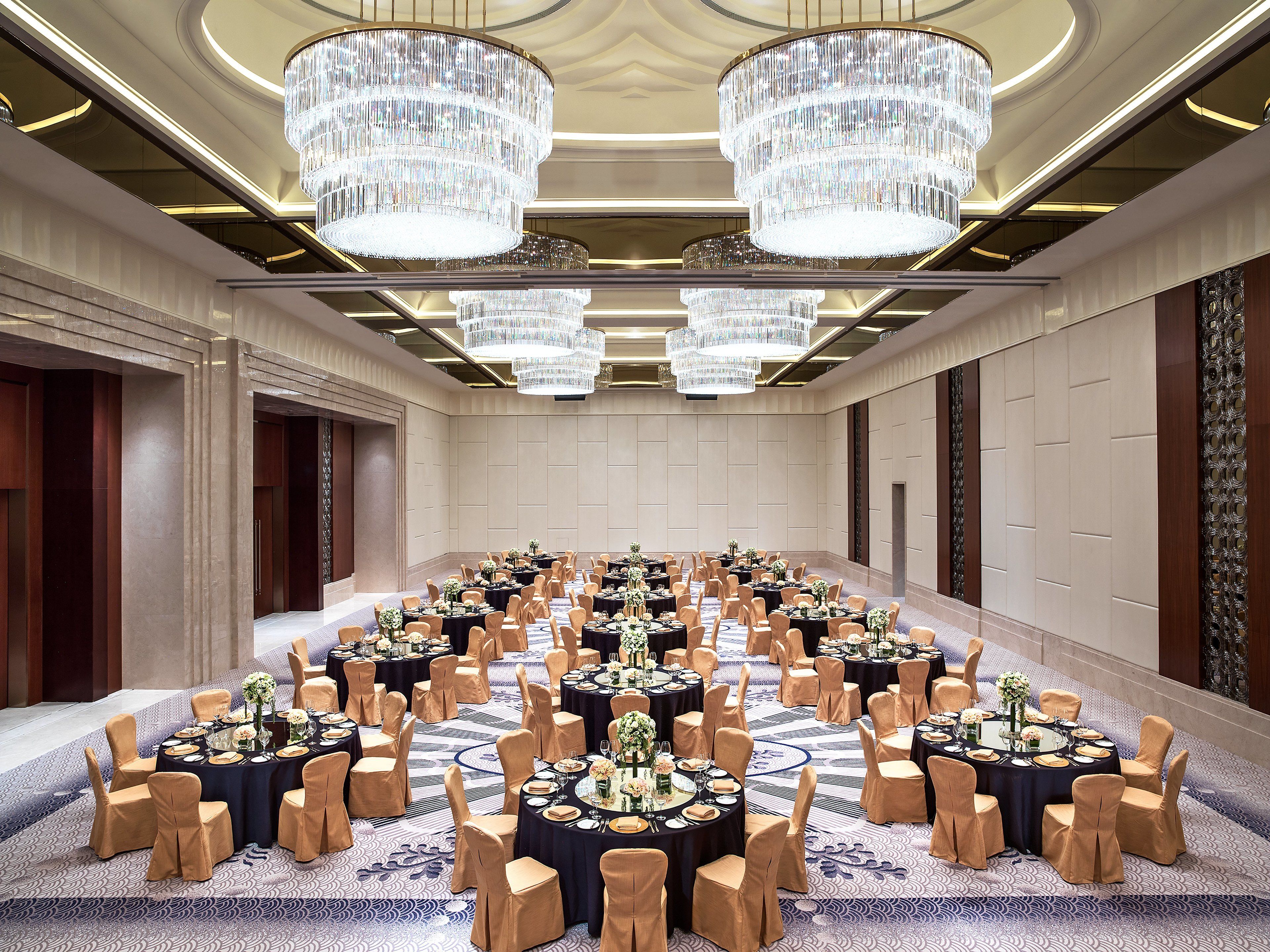 Une grande salle de conférence équipée de tables rondes, de chaises et de lustres.