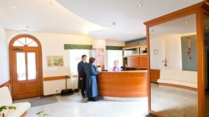 A reception area with a wooden reception desk, a waiting area with a sofa, and a large arched doorway. - Hotel Reza (Frantiskovy Lazne)