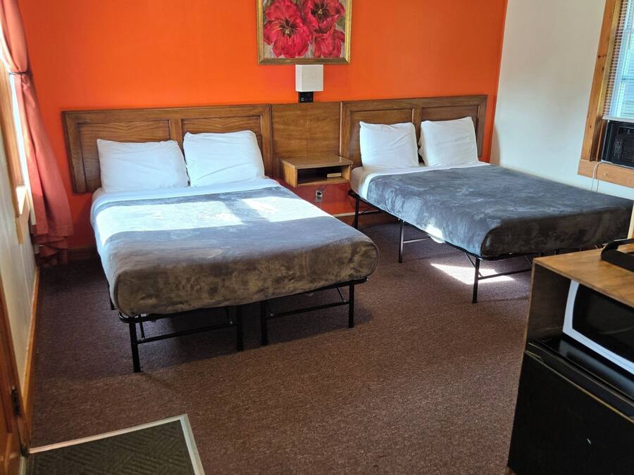 Habitación de hotel con dos camas, un cabecero de madera, un cuadro de flores, una mesita de noche de madera y una zona de kitchenette.