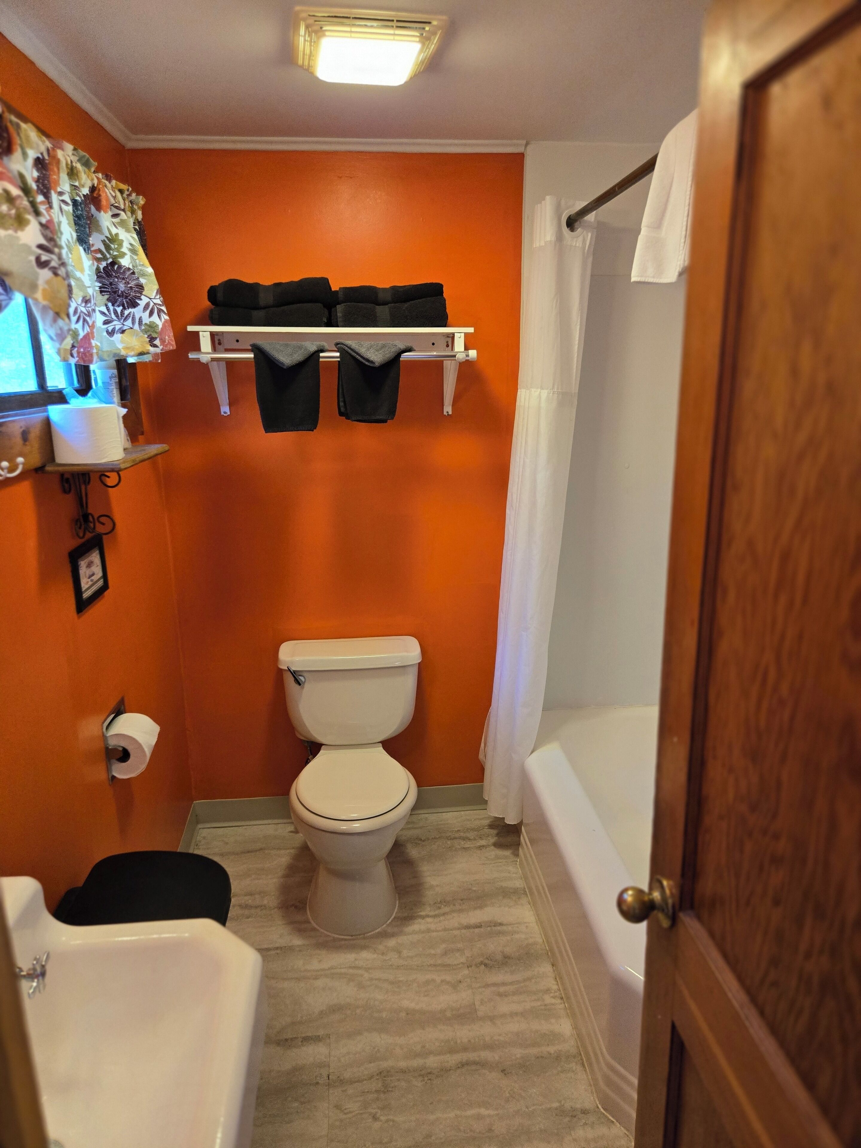 A bathroom with an orange wall, a white toilet, a white bathtub, and a shower curtain.