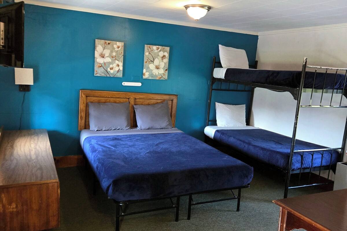 A room with two beds, a desk, and a bunk bed. There are two wall-mounted lamps and a ceiling light.